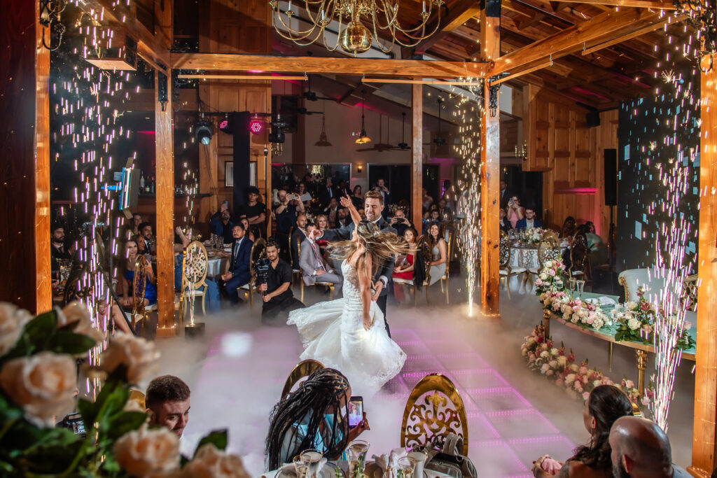 A wedding first dance beneath The Tavern's wood beams and chandeliers, surrounded by guests
