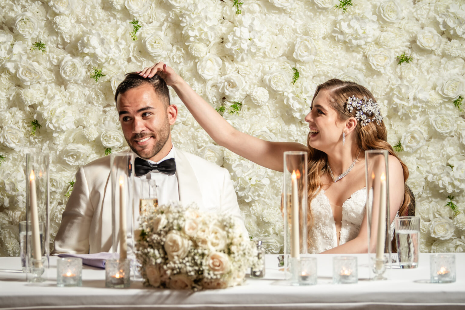 A smiling couple at their candlelit sweetheart table with white flowers in The Tavern