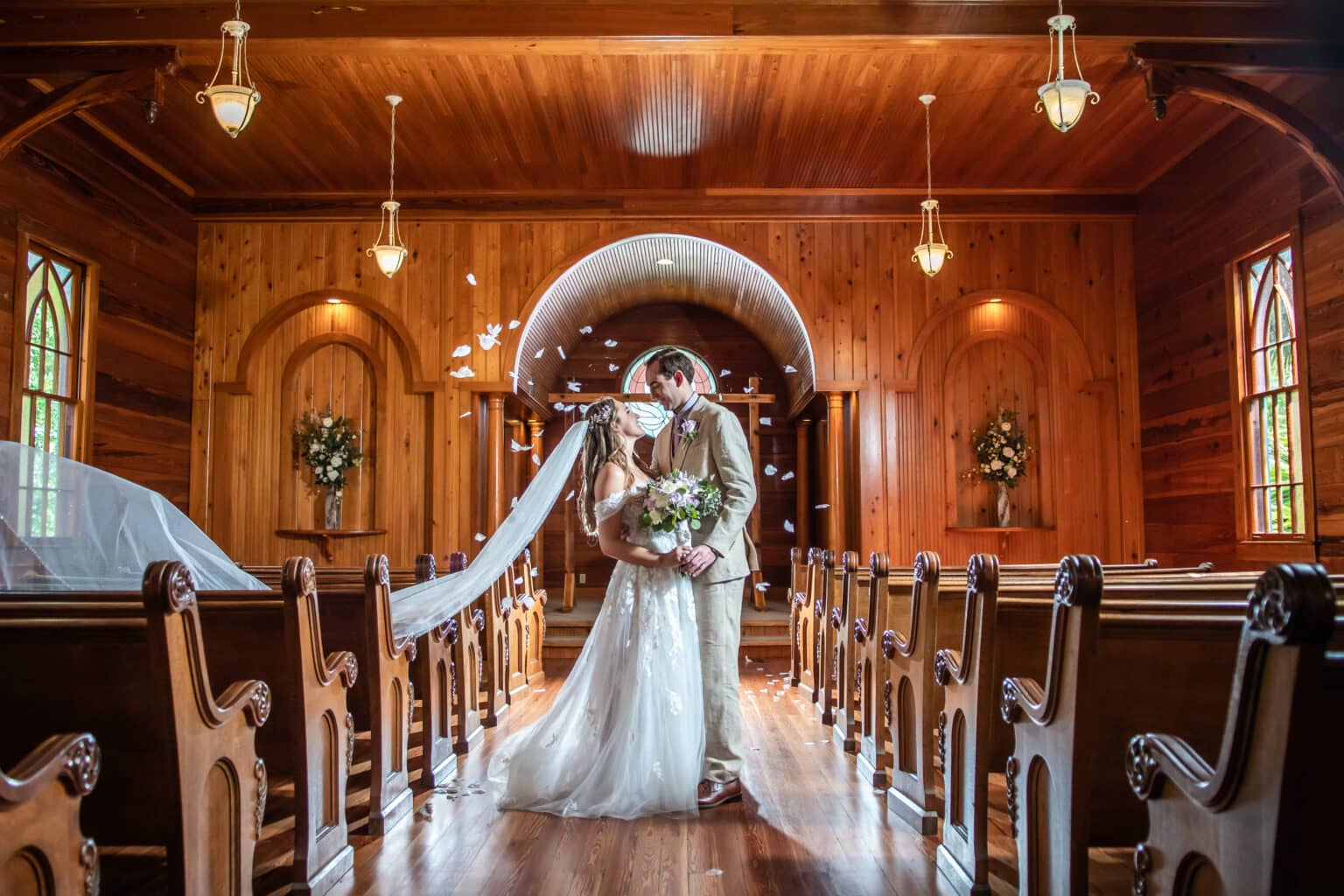 Newlyweds kissing in the wood-paneled Chapel aisle between curved wooden pews
