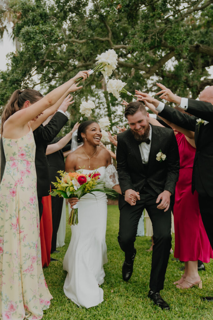 Newlyweds laughing as their wedding party raises bouquets above them on the estate lawn