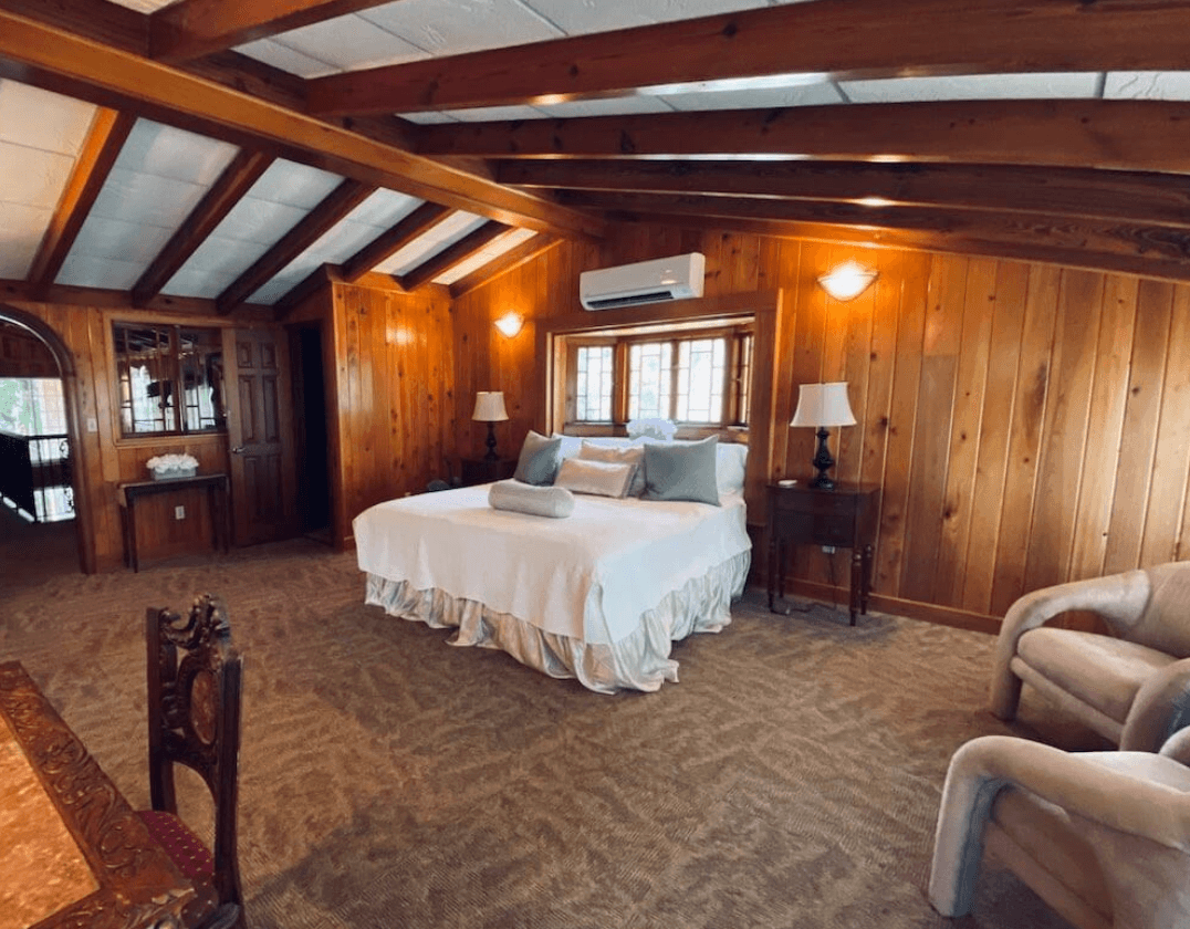 Wood-paneled bridal suite bedroom with exposed ceiling beams and a sitting area at Agatha’s Guesthouse